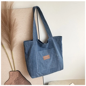 Detail of blue denim tote bag featuring a leather logo patch and a practical outer pocket