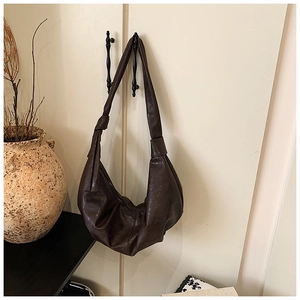 Detail view of a large brown leather croissant bag with stylish knotted shoulder strap