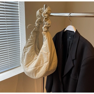 Detail of cream quilted crescent bag featuring ruched shoulder strap and puffer nylon texture