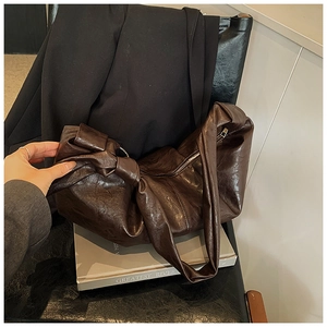 Detail of dark brown leather slouchy bag featuring a stylish wide strap knot and silver zipper