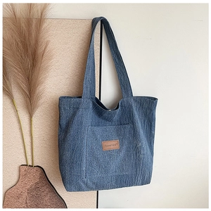 Detail of blue denim canvas tote bag featuring brown leather logo and front pocket
