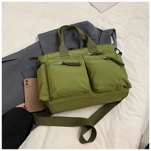 Detail of olive green nylon tote bag featuring front zip pockets and woven pullers