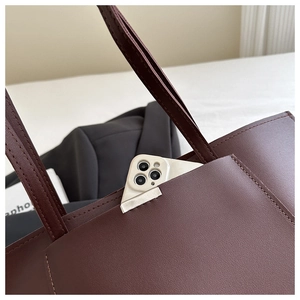 Close-up of red-brown leather tote bag showing textured finish and front pocket detail