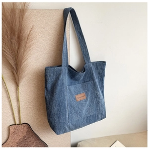 Detail of blue denim tote bag showing the front pocket and brown leather brand patch