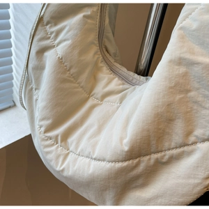 Detail of oat-colored quilted nylon crescent bag with curved stitching and zipper
