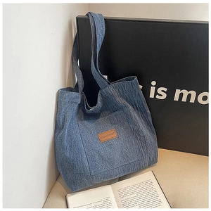 Detail of blue denim canvas tote bag with brown leather label and dual shoulder straps