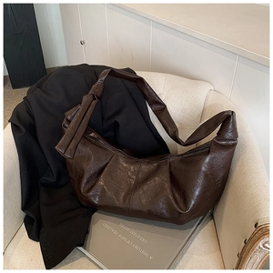 Detail of a dark brown crescent bag with pleated leather texture and a knotted strap detail