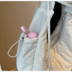Detail of quilted puffer bag showing side drawstring pocket and metallic zipper closure