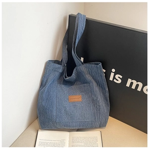 Detail view of denim canvas tote bag featuring a front pocket and leather logo patch