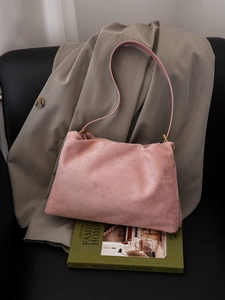 Detail of pink suede Boston bag with slim shoulder strap on an olive green book