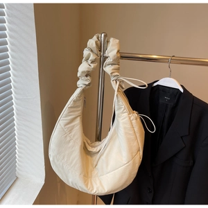 Detail of cream quilted crescent bag featuring a ruffled cloud strap and nylon texture