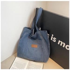 Detail view of the blue fabric tote bag featuring a brown leather brand patch on the pocket