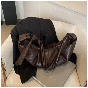 Detail of dark brown leather crescent bag with knotted shoulder strap on a beige sofa