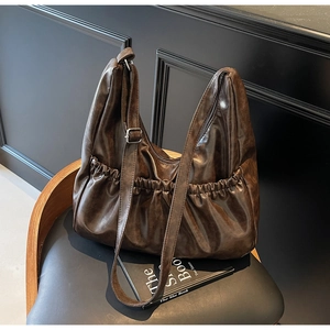 Nahaufnahme einer braunen Vintage-Falten-Tote-Bag mit verstellbarem Gurt auf einem Stuhl