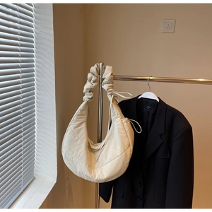 Detail of quilted beige down shoulder bag featuring ruched cloud-style strap and crescent shape