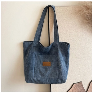 Detail view of washed blue denim tote bag with front pocket and leather Speed Mail patch