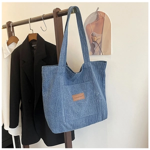 Close-up of a blue denim canvas tote bag with a brown leather logo patch and wide strap