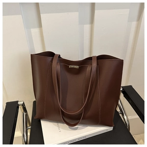 Detailed shot of dark brown tote bag on chair showing smooth leather texture and gold buckle