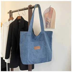 Close-up of blue denim canvas tote bag featuring brown leather tag and front pocket detail