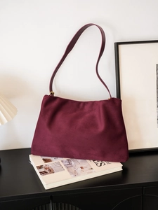 Close-up of a burgundy suede Boston shoulder bag resting on a black cabinet in a room