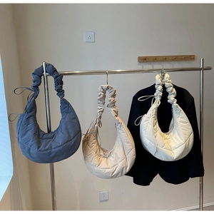 Three quilted puffer dumpling bags in blue-gray, beige, and cream with pleated straps