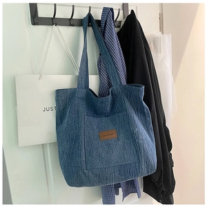 Close-up of indigo denim tote bag with brown leather label and functional front pocket
