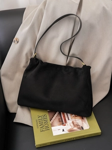 Detail of minimalist black suede bag with gold hardware ring on beige blazer