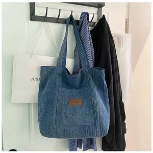 Detail view of denim canvas tote bag featuring brown leather logo and large front pocket
