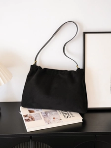 Minimalist black suede shoulder bag with gold hardware and soft pleated texture