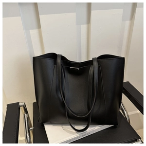 Detail of a large black minimalist tote bag with metal logo on a modern black chair