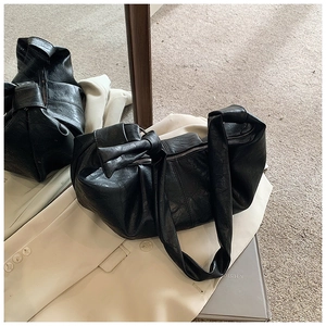 Close-up of black pleated faux leather shoulder bag with decorative knotted strap detail