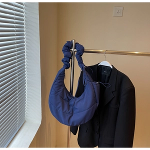 Detail of navy quilted nylon shoulder bag with pleated strap on a minimalist metal hanger