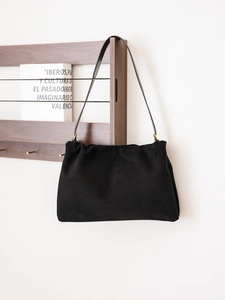 Macro view of black suede Boston bag with delicate gold hardware and soft pleated texture
