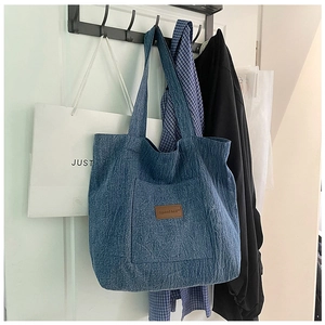 Detailed view of blue denim tote bag featuring external pocket and brown leather label