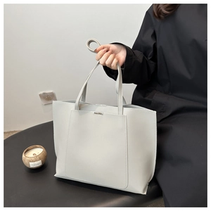 Detail of light gray tote bag featuring a structured rectangular shape and metal trim