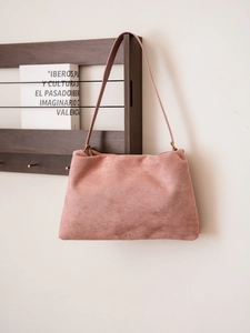 Detail view of pink suede shoulder bag showing smooth texture on wooden shelf