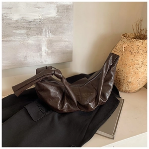 Close-up of dark brown crescent bag with pleated leather texture and knotted strap detail