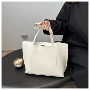 Detail of minimalist cream leather tote bag with elegant metal accent and long strap