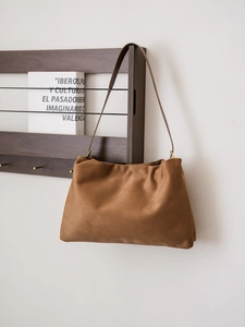 Detailed close-up of brown suede hobo bag with gold ring hardware on a wooden stand