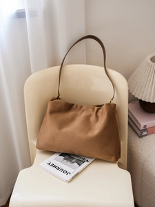 Detail of dark brown suede Boston bag with minimalist pleats on a cream chair