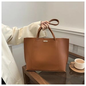 Close-up of brown tote bag showing the front pocket, silver bar detail, and adjustable strap