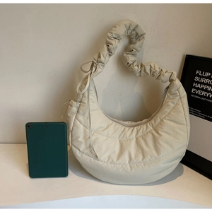 Detailed view of cream quilted puffer bag with pleated strap next to a tablet for scale