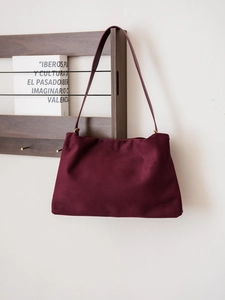Close-up of a burgundy suede Boston bag hanging on a minimalist wooden shelf