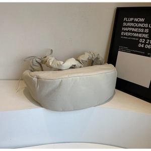 Detail of a puffy cream crescent bag with cloud-like gathered handle on a white stand