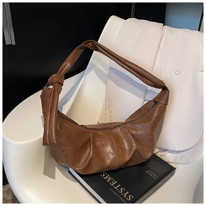 Detail of a brown leather dumpling bag featuring soft pleats and a decorative side knot