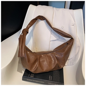 Close-up of brown textured leather crescent bag with stylish ruched design and knotted strap