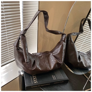 Close-up of brown crescent bag with retro pleated faux leather and knot shoulder strap detail