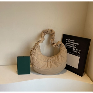 Detail of beige quilted crescent shoulder bag with pleated strap on display stand