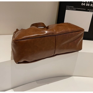 Nahaufnahme der Bodennähte und der weichen Faltenstruktur dieser braunen PU-Handtasche