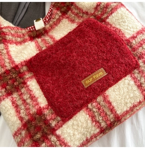 Detail of plush red plaid tote bag featuring a lamb wool texture and leather label